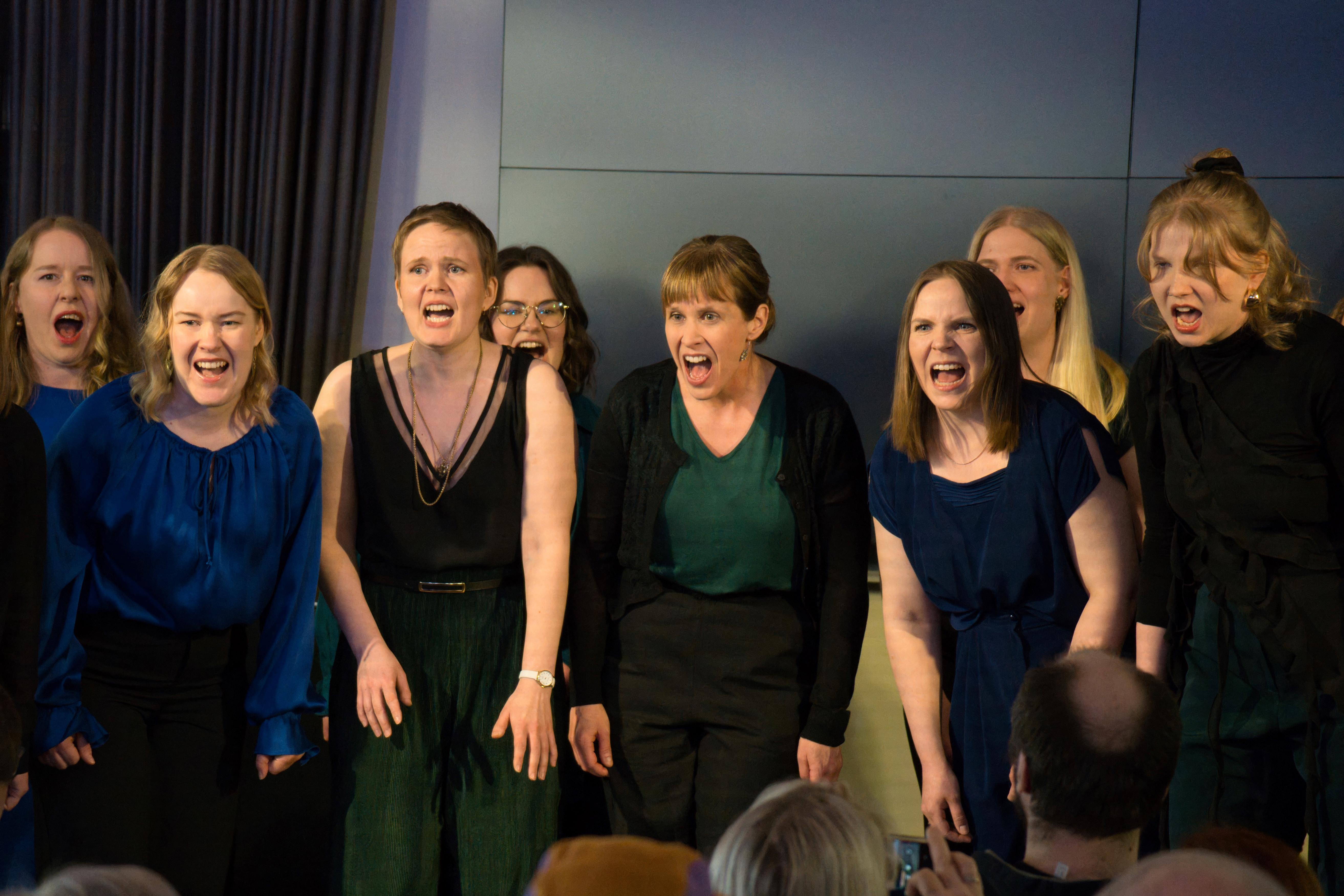 Group of white young women singing with intense feeling in a dark room.