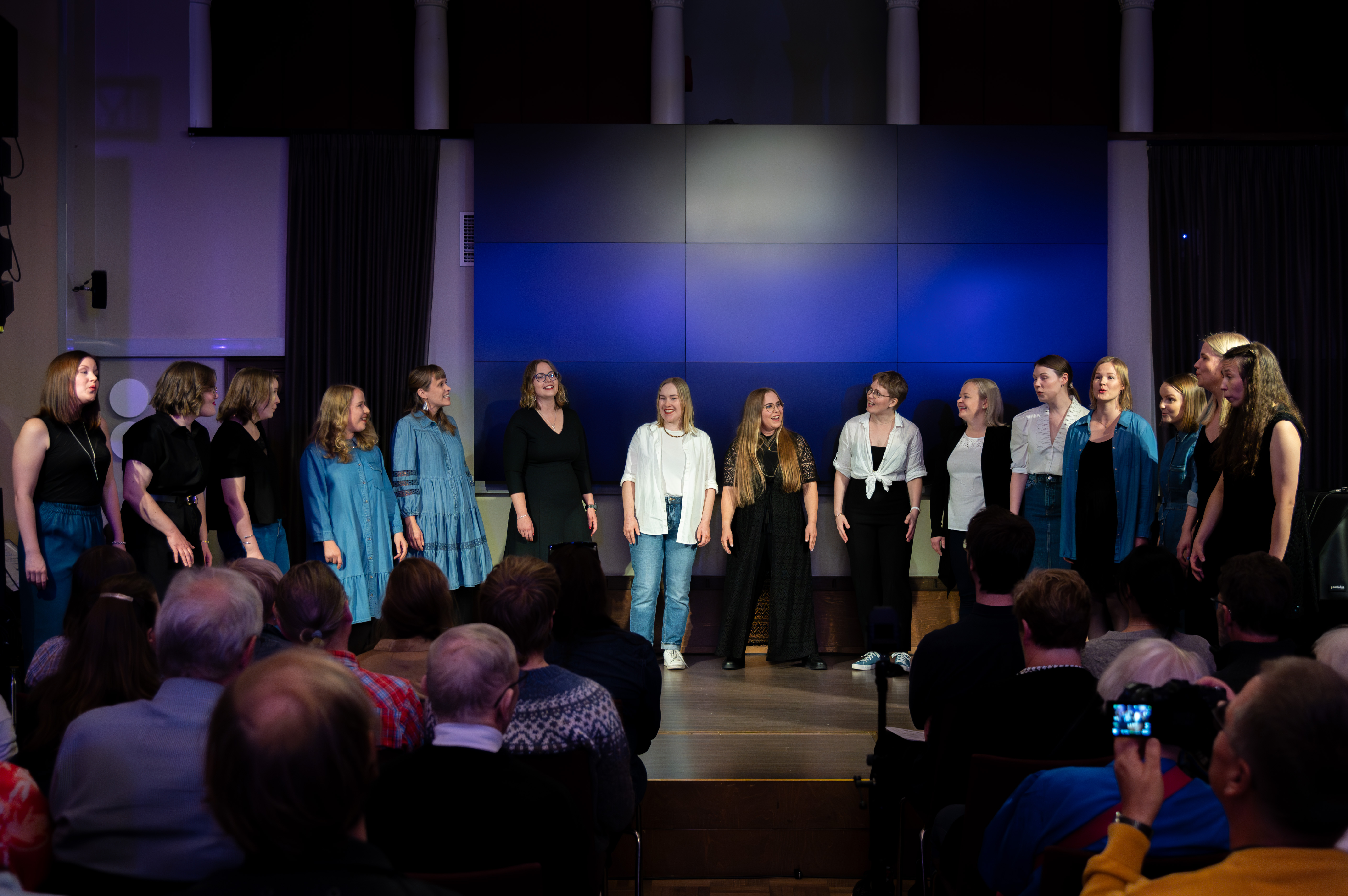Group of women singing in a dark space in front of an audience.