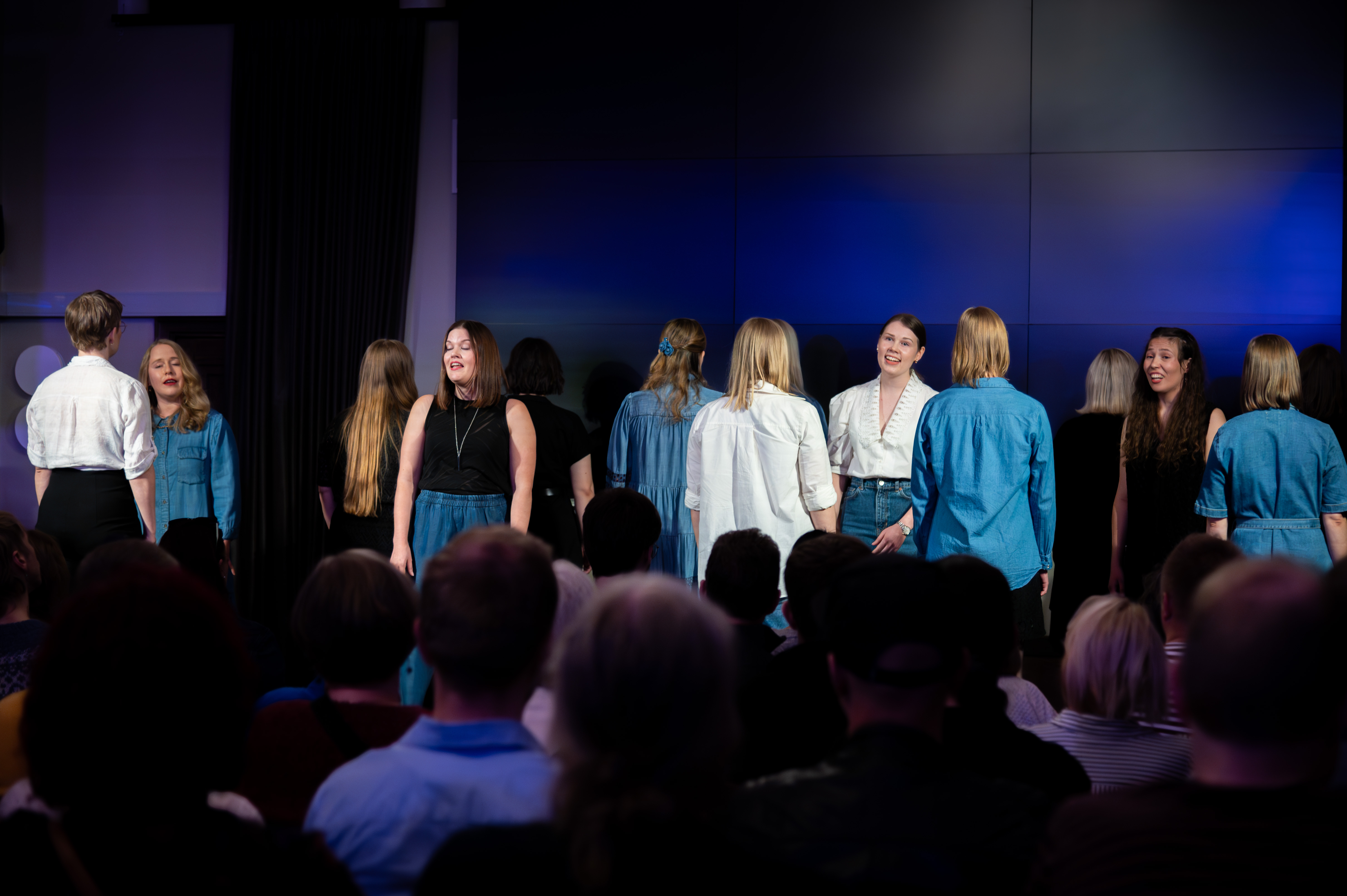 Group of women singing in a dark space in front of an audience.