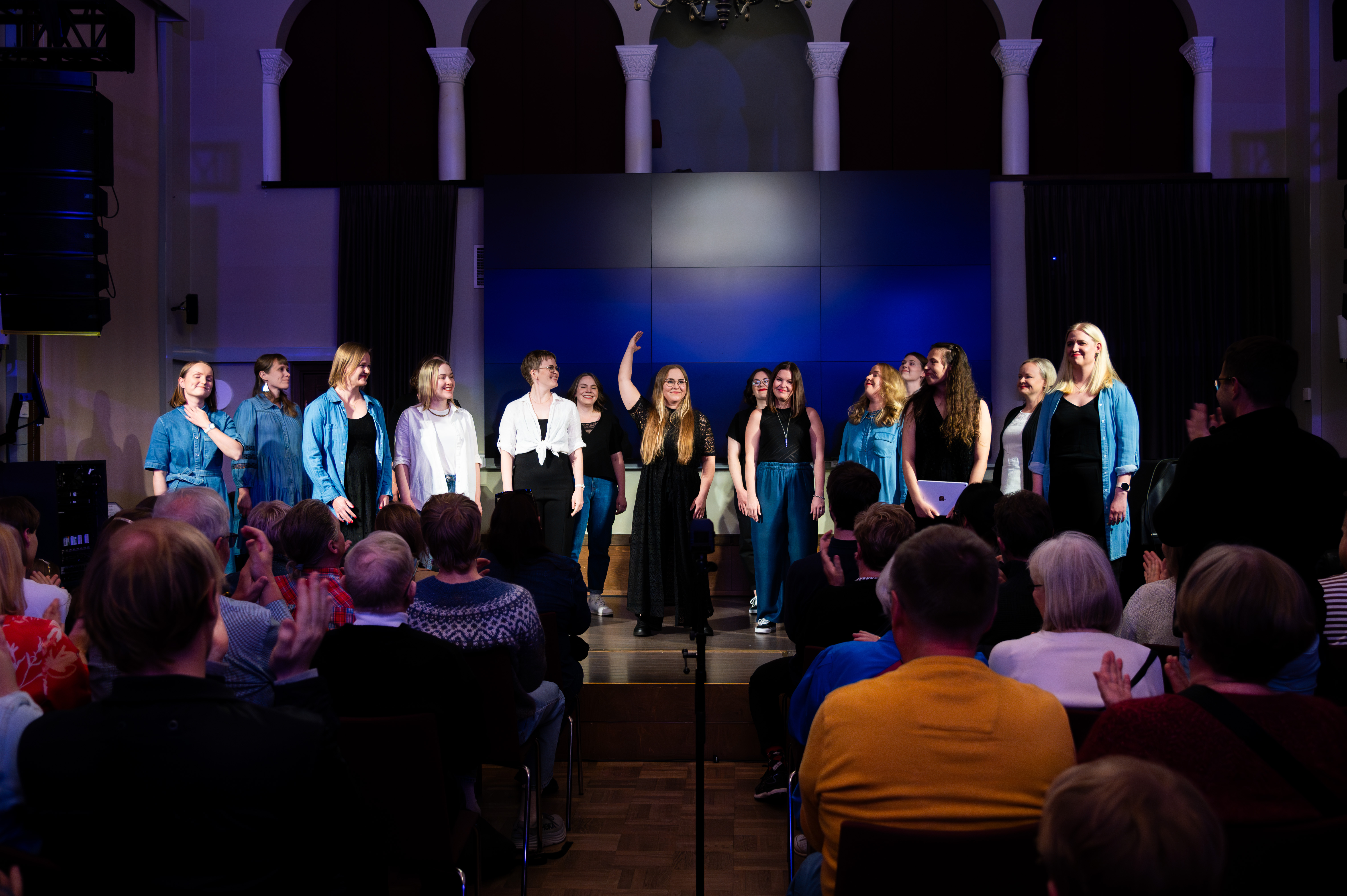 Group of women singing in a dark space in front of an audience.